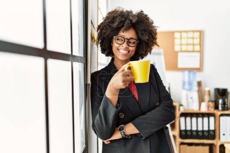 Foto de Joven mujer afroamericana sonriendo confiado bebiendo café en la oficina - Imagen libre de derechos