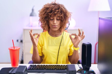 Téléchargez les photos : Young hispanic woman with curly hair playing video games wearing headphones relax and smiling with eyes closed doing meditation gesture with fingers. yoga concept. - en image libre de droit