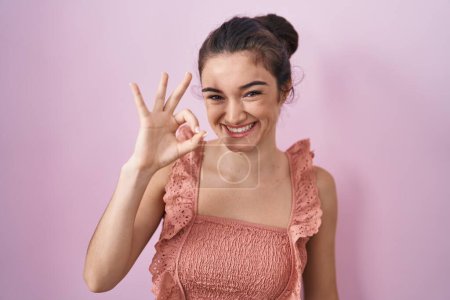 Téléchargez les photos : Young teenager girl standing over pink background smiling positive doing ok sign with hand and fingers. successful expression. - en image libre de droit