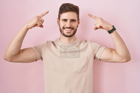 Foto de Hombre hispano con barba de pie sobre fondo rosa sonriendo señalando a la cabeza con ambas manos dedo, gran idea o pensamiento, buena memoria - Imagen libre de derechos