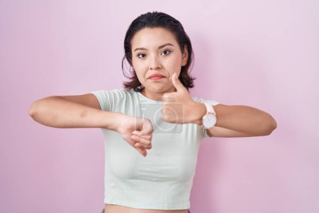 Photo for Hispanic young woman standing over pink background doing thumbs up and down, disagreement and agreement expression. crazy conflict - Royalty Free Image