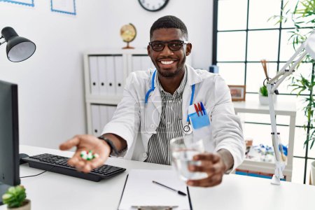 Photo for Young african american man wearing doctor uniform holding pills at clinic - Royalty Free Image