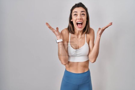 Foto de Hispanic woman wearing sportswear over isolated background celebrating mad and crazy for success with arms raised and closed eyes screaming excited. winner concept - Imagen libre de derechos