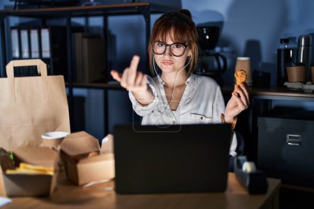 Photo for Young beautiful woman working using computer laptop and eating delivery food showing middle finger, impolite and rude fuck off expression - Royalty Free Image