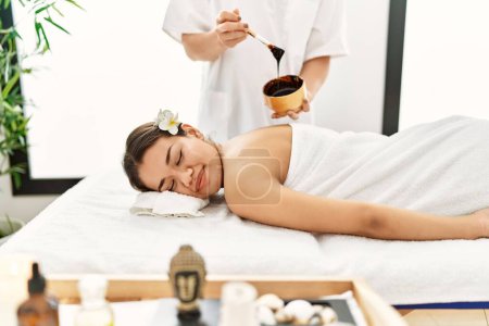 Photo for Young latin woman relaxed having back massage with chocolate therapy at beauty center - Royalty Free Image
