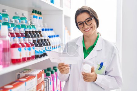Foto de Joven farmacéutica hispana sosteniendo frasco de prescripción y pastillas en farmacia - Imagen libre de derechos