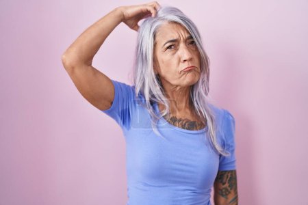Photo for Middle age woman with tattoos standing over pink background confuse and wondering about question. uncertain with doubt, thinking with hand on head. pensive concept. - Royalty Free Image