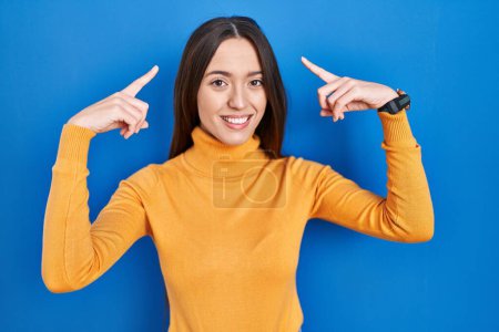 Photo for Young brunette woman standing over blue background smiling pointing to head with both hands finger, great idea or thought, good memory - Royalty Free Image