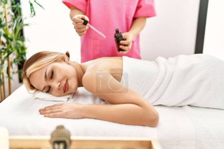 Téléchargez les photos : Jeune femme caucasienne allongée sur la table ayant massage du dos à l'huile au salon de beauté - en image libre de droit