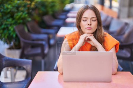 Téléchargez les photos : Jeune femme utilisant un ordinateur portable avec l'expression du doute à la terrasse du café - en image libre de droit