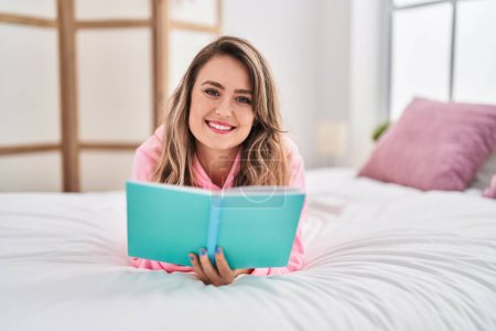 Photo for Young woman reading book lying on bed at bedroom - Royalty Free Image