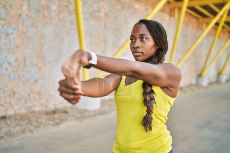 Photo for African american woman wearing sportswear stretching arm at street - Royalty Free Image
