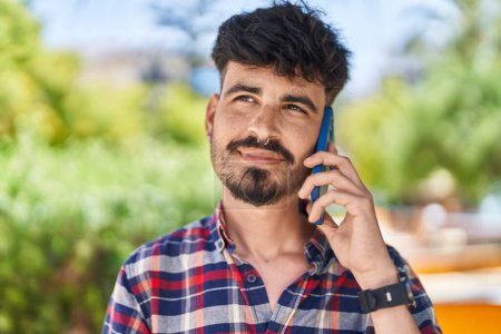 Téléchargez les photos : Jeune homme hispanique souriant confiant parler sur le smartphone au parc - en image libre de droit