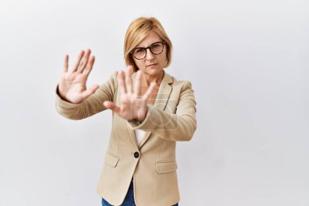 Foto de Mujer de negocios rubia de mediana edad de pie sobre un fondo aislado haciendo marco usando las manos palmas y los dedos, perspectiva de la cámara - Imagen libre de derechos