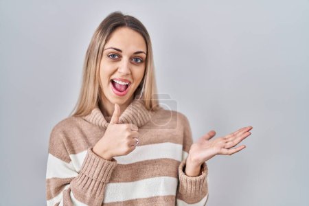 Téléchargez les photos : Young blonde woman wearing turtleneck sweater over isolated background showing palm hand and doing ok gesture with thumbs up, smiling happy and cheerful - en image libre de droit