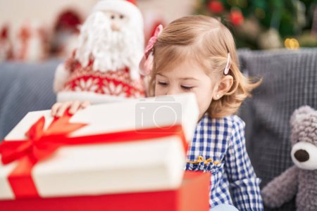 Foto de Adorable chica hispana desempacando regalo sentado en el sofá por el árbol de Navidad en casa - Imagen libre de derechos