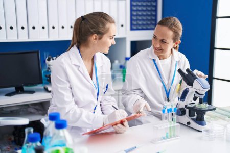 Photo for Two women scientists using microscope and write on document at laboratory - Royalty Free Image