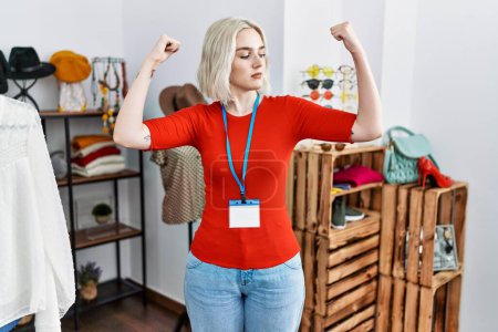 Téléchargez les photos : Young caucasian woman working as manager at retail boutique showing arms muscles smiling proud. fitness concept. - en image libre de droit