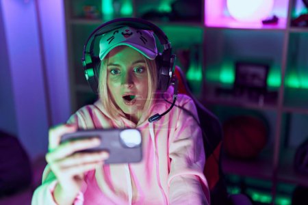 Téléchargez les photos : Young caucasian woman playing video games with smartphone pointing thumb up to the side smiling happy with open mouth - en image libre de droit