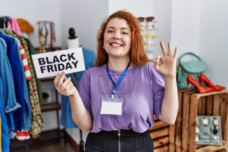 Foto de Young redhead woman holding black friday banner at retail shop doing ok sign with fingers, smiling friendly gesturing excellent symbol - Imagen libre de derechos