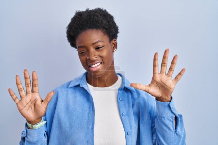 Téléchargez les photos : Femme afro-américaine debout sur fond bleu montrant et pointant vers le haut avec les doigts numéro dix tout en souriant confiant et heureux. - en image libre de droit