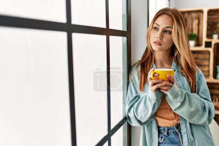 Young caucasian woman drinking coffee standing at home