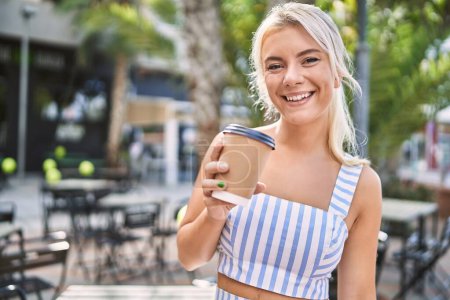 Téléchargez les photos : Jeune fille blonde souriant heureux boire du café à la ville. - en image libre de droit