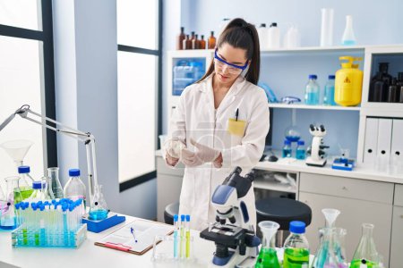 Photo for Young beautiful hispanic woman scientist wearing gloves at laboratory - Royalty Free Image