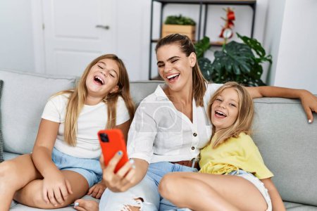 Photo for Mother and daughters smiling confident making selfie by the smartphone at home - Royalty Free Image
