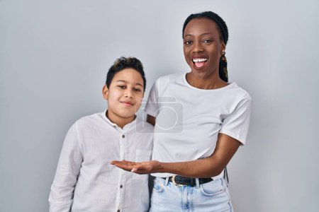 Téléchargez les photos : Young mother and son standing together over white background pointing aside with hands open palms showing copy space, presenting advertisement smiling excited happy - en image libre de droit