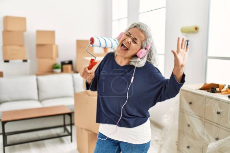 Photo for Middle age grey-haired woman listening to music and singing at new home. - Royalty Free Image