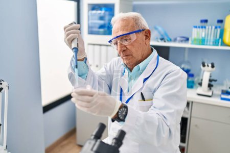 Photo for Senior man wearing scientist uniform using pipette working at laboratory - Royalty Free Image