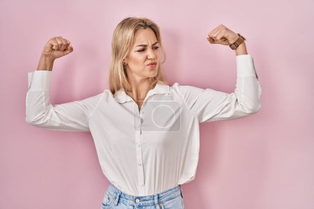 Foto de Young caucasian woman wearing casual white shirt over pink background showing arms muscles smiling proud. fitness concept. - Imagen libre de derechos