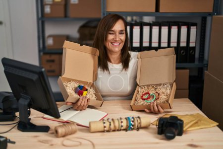 Foto de Middle age woman working at small bracelets business ecommerce winking looking at the camera with sexy expression, cheerful and happy face. - Imagen libre de derechos