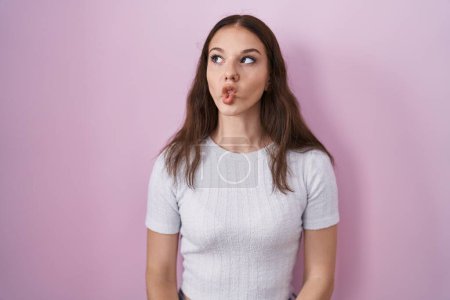 Téléchargez les photos : Young hispanic girl standing over pink background making fish face with lips, crazy and comical gesture. funny expression. - en image libre de droit