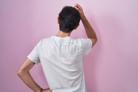 Téléchargez les photos : Young hispanic man standing over pink background backwards thinking about doubt with hand on head - en image libre de droit