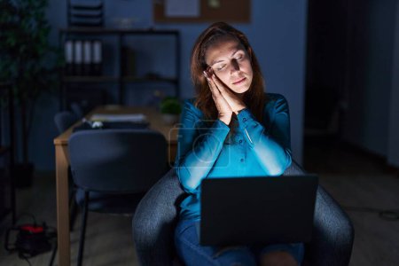 Téléchargez les photos : Brunette woman working at the office at night sleeping tired dreaming and posing with hands together while smiling with closed eyes. - en image libre de droit