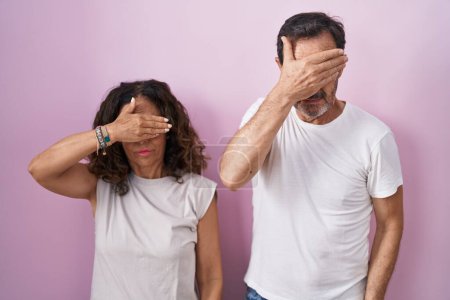 Photo for Middle age hispanic couple together over pink background covering eyes with hand, looking serious and sad. sightless, hiding and rejection concept - Royalty Free Image