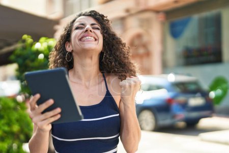 Téléchargez les photos : Jeune belle femme hispanique utilisant touchpad avec expression gagnante dans la rue - en image libre de droit