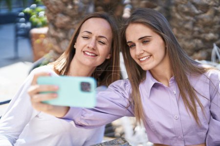 Foto de Dos mujeres madre e hija hacen selfie por teléfono inteligente sentado en la mesa en la terraza de la cafetería - Imagen libre de derechos
