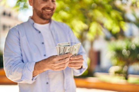 Photo for Young caucasian man smiling confident counting dollars at park - Royalty Free Image
