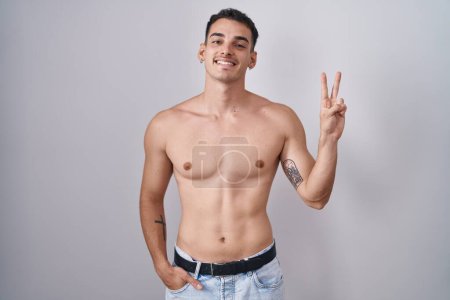 Photo for Handsome hispanic man standing shirtless smiling with happy face winking at the camera doing victory sign with fingers. number two. - Royalty Free Image