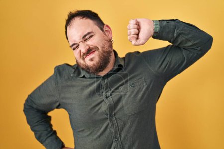 Photo for Plus size hispanic man with beard standing over yellow background stretching back, tired and relaxed, sleepy and yawning for early morning - Royalty Free Image