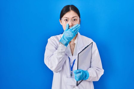 Téléchargez les photos : Jeune femme chinoise travaillant au laboratoire scientifique choqué couvrant la bouche avec les mains pour erreur. concept secret. - en image libre de droit