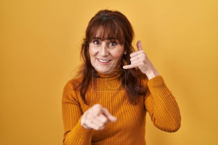 Téléchargez les photos : Femme hispanique du Moyen Âge debout sur fond jaune souriant faire parler au téléphone geste et vous pointant du doigt. Appelle-moi. - en image libre de droit