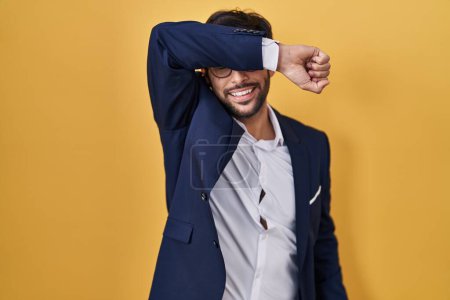 Photo for Handsome latin man standing over yellow background covering eyes with arm smiling cheerful and funny. blind concept. - Royalty Free Image