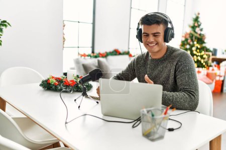 Photo for Young hispanic man radio worker working sitting by christmas tree at home - Royalty Free Image
