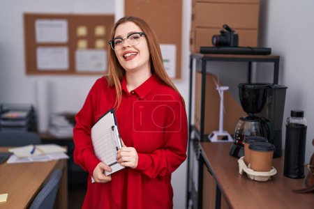 Téléchargez les photos : Young redhead woman business worker smiling confident holding clipboard at office - en image libre de droit