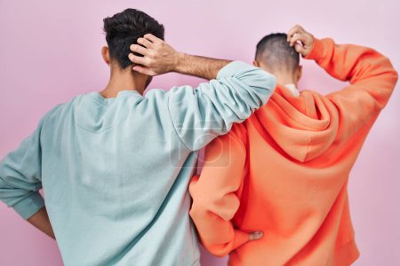 Foto de Joven pareja gay hispana de pie sobre fondo rosa al revés pensando en la duda con la mano en la cabeza - Imagen libre de derechos
