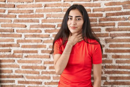 Téléchargez les photos : Young teenager girl standing over bricks wall touching painful neck, sore throat for flu, clod and infection - en image libre de droit